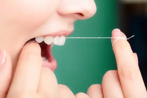 woman flossing teeth green background